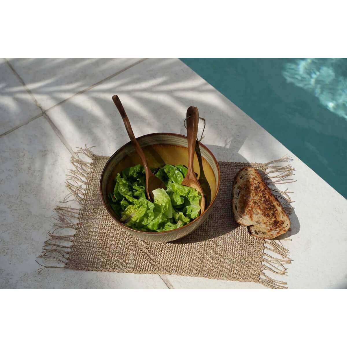 Een natuurlijke placemat van zeegras met een saladeschaal en brood bij het zwembad.