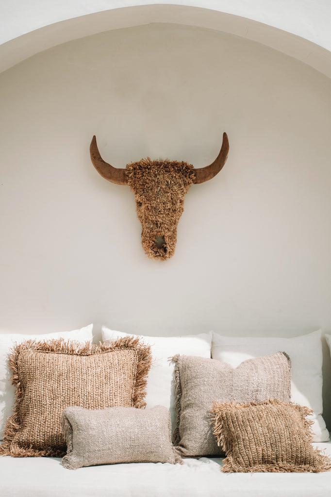 Gezellige zithoek met beige boho kussenhoezen en decoratieve buffelschedel aan de muur voor een chique interieurstijl.