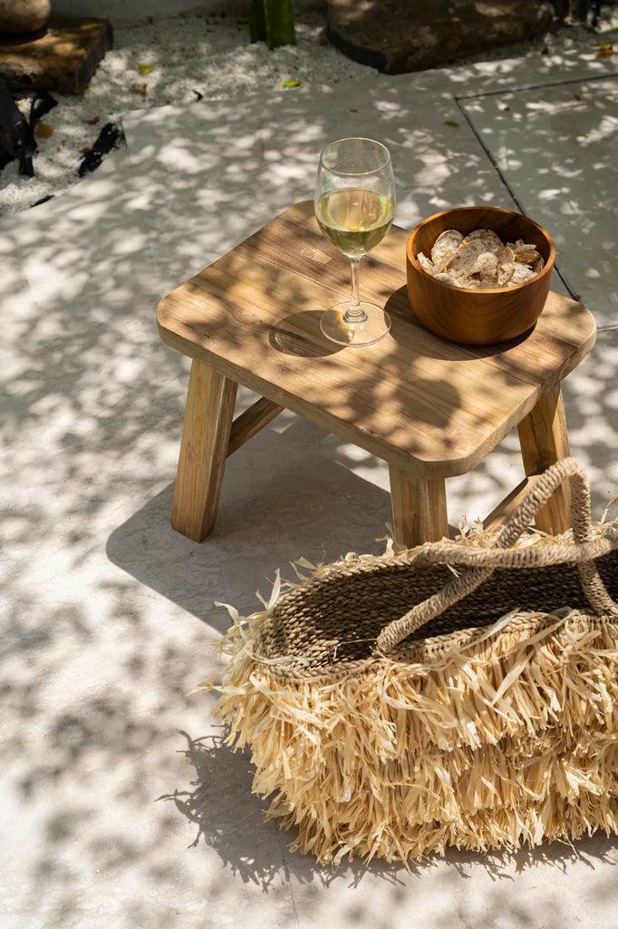 De Quincy Kruk - Naturel als stijlvolle bijzettafel met glas wijn en schaal snacks, in een zonnige tuin met schaduwspel.