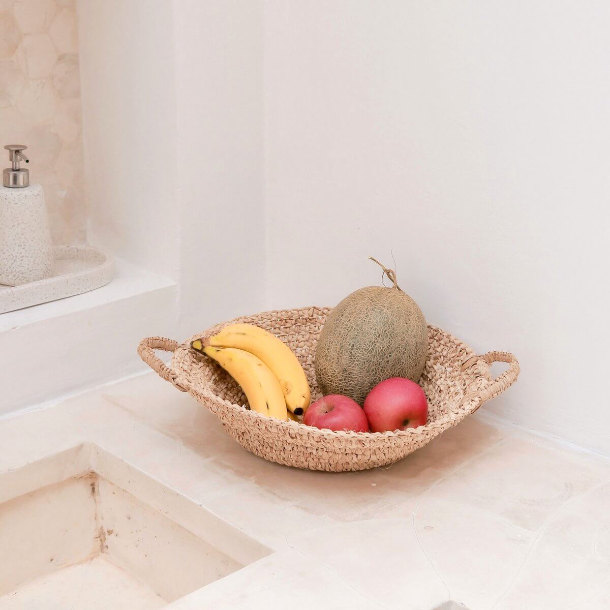 Handgemaakte raffia fruitschaal met bananen, meloen en appels, ideaal voor keuken of eettafel, duurzaam en decoratief.