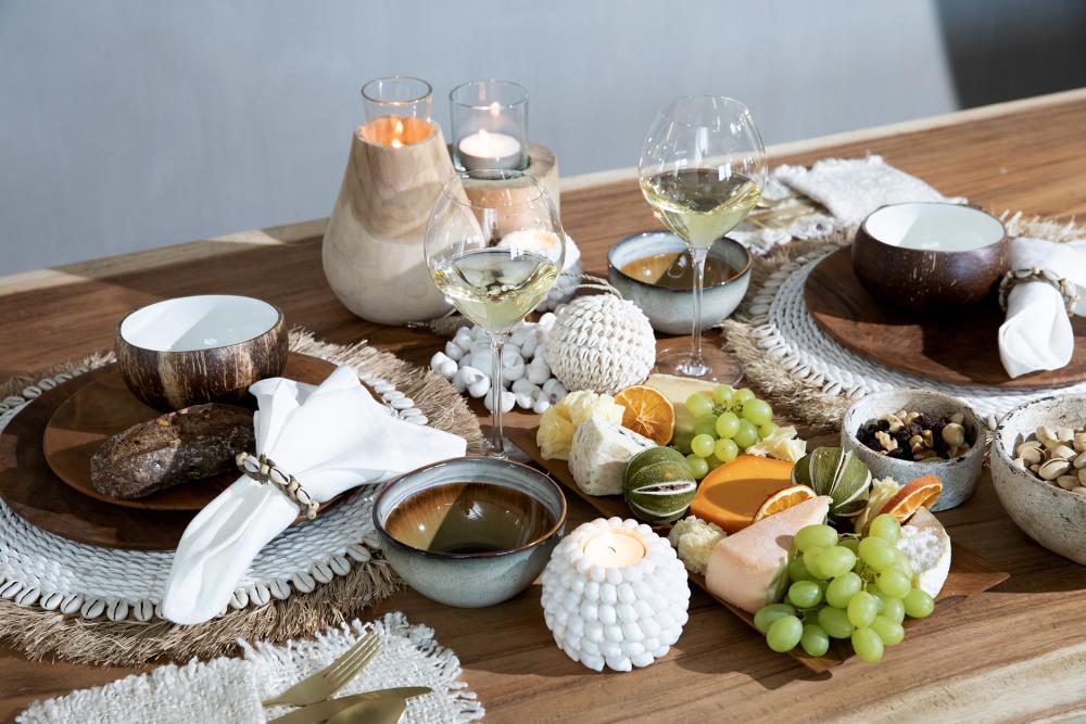 Tropische tafelsetting met zeegras placemats en kauri schelpen, boho sfeer met wit en natuurlijke tinten voor gezelligheid.