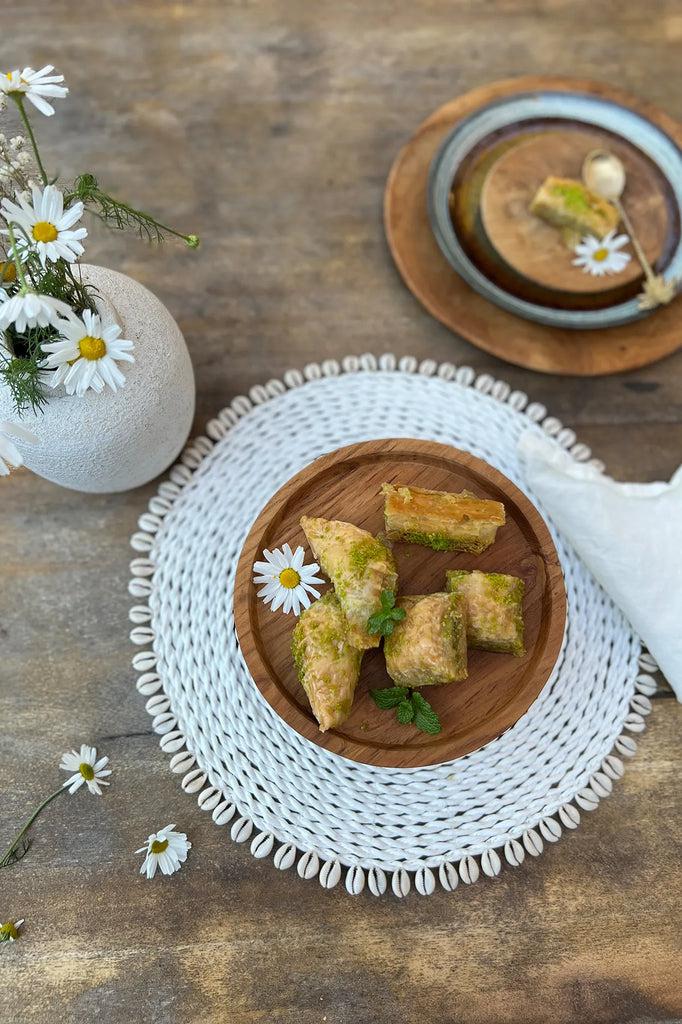 Aan tafel met ambachtelijke zeegras placemat met kauri schelpen en snacks, omringd door bloeiende madeliefjes.