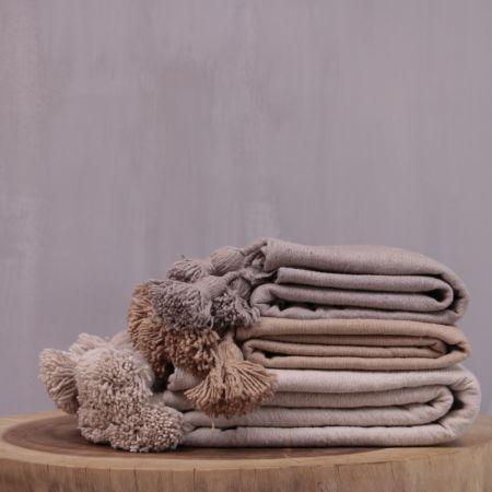 Gestapelde pompom dekens in camelkleur op een houten tafel, perfect voor een modern of boho interieur.